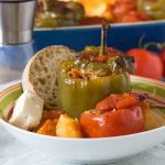 A colourful dish of Greek stuffed tomatoes and peppers with bread and feta - there's a baking dish in the background