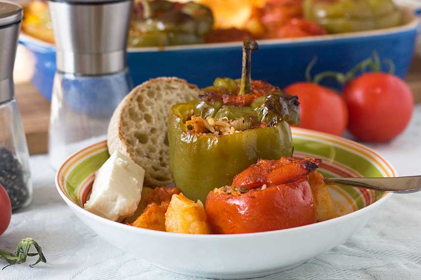 A colourful dish of Greek stuffed tomatoes and peppers with bread and feta - there's a baking dish in the background