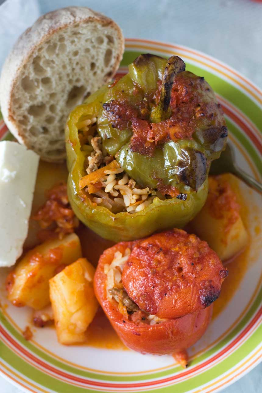 An overhead shot of Greek stuffed tomatoes and peppers in a colourful dish with bread and feta cheese