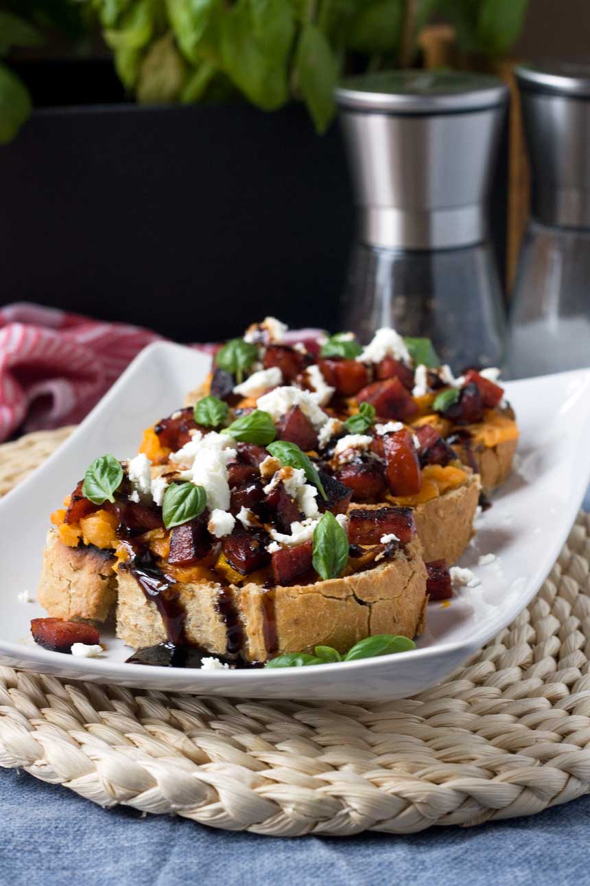 A close up of a platter of Bruschetta with sweet potato and chorizo on a wicker mat. 