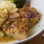 A closeup of baked honey mustard chicken and potatoes in a white bowl.