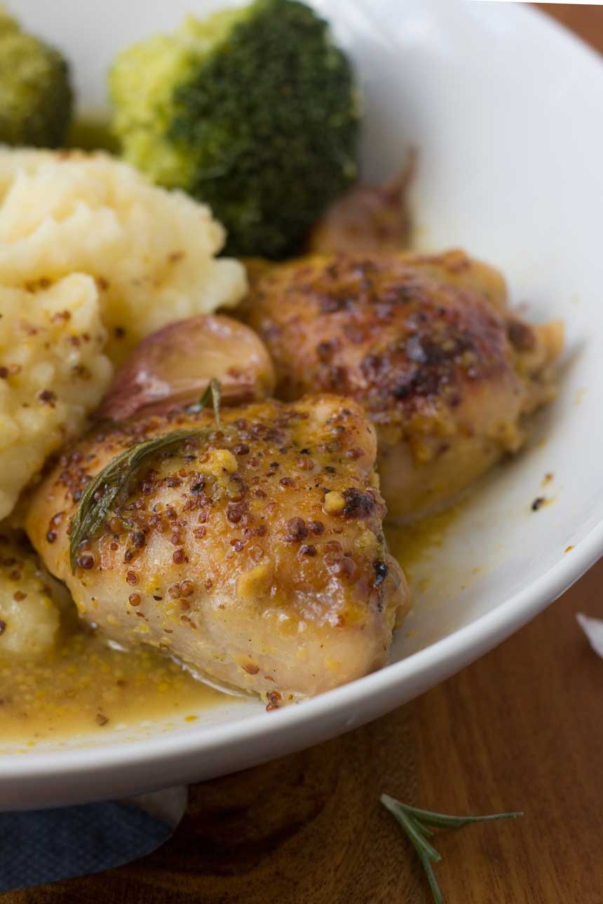 A closeup of baked honey mustard chicken and potatoes in a white bowl.