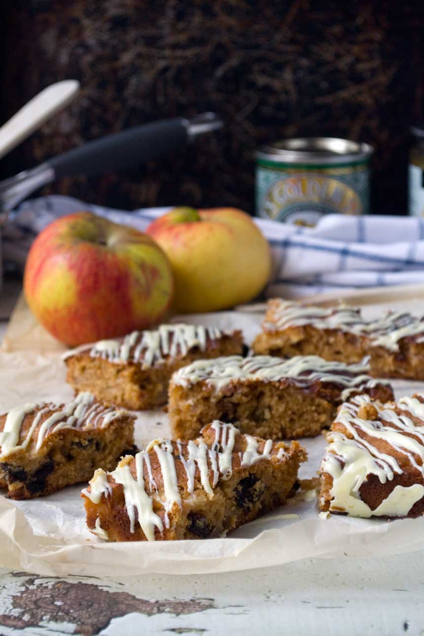 sticky apple ginger cake bars on baking paper with apples and other ingredients in the background