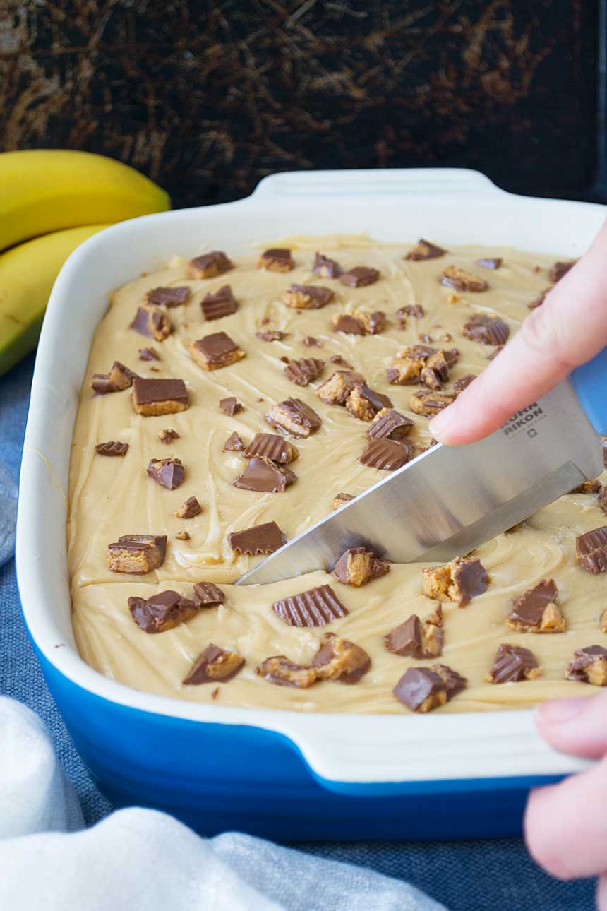 Someone slicing into Banana sheet cake with peanut butter fudge frosting with a big knife.
