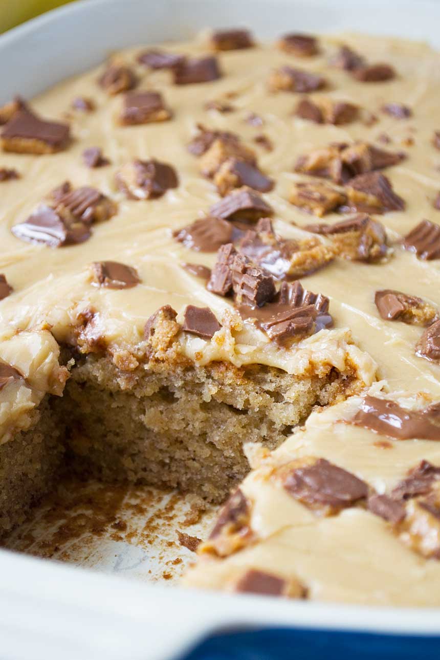 A close up of banana cake with peanut butter frosting and peanut butter cups on top with a big piece cut out.