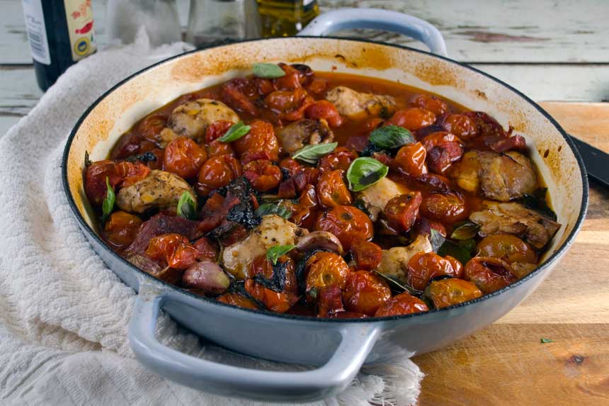 Baked chicken and chorizo with cherry tomatoes in a round blue cast iron pan.