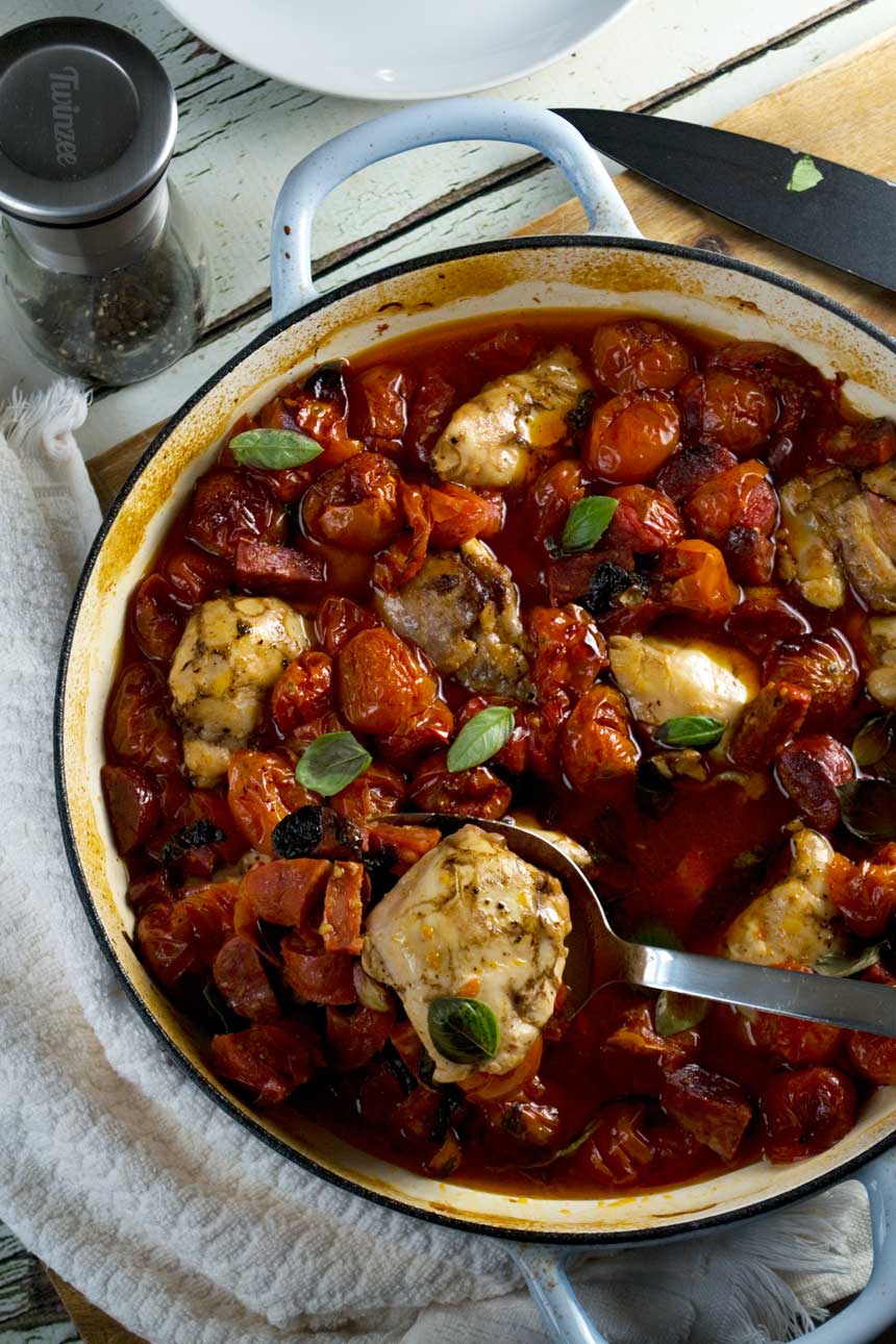 A closeup of a pan of baked chicken and chorizo with a spoon in it taken from above.