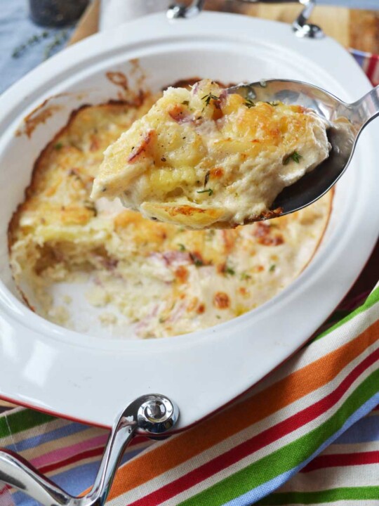 Someone holding up a spoonful of creamy garlic parmesan potatoes (dauphinoise potatoes) over the baking dish