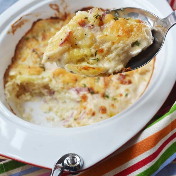 Someone holding up a spoonful of creamy garlic parmesan potatoes (dauphinoise potatoes) over the baking dish