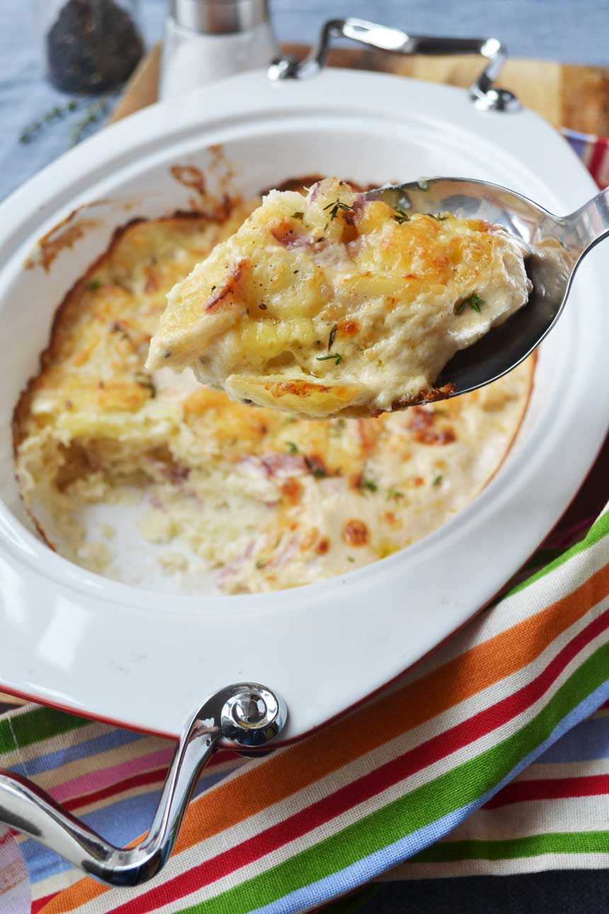 Someone holding up a spoonful of creamy garlic parmesan potatoes (dauphinoise potatoes) over the baking dish