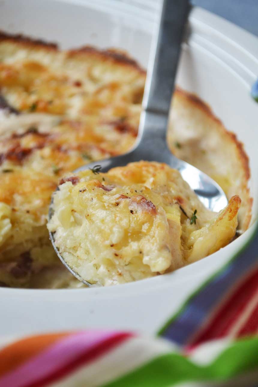 A closeup of a spoon of creamy garlic parmesan potatoes being held above the baking dish