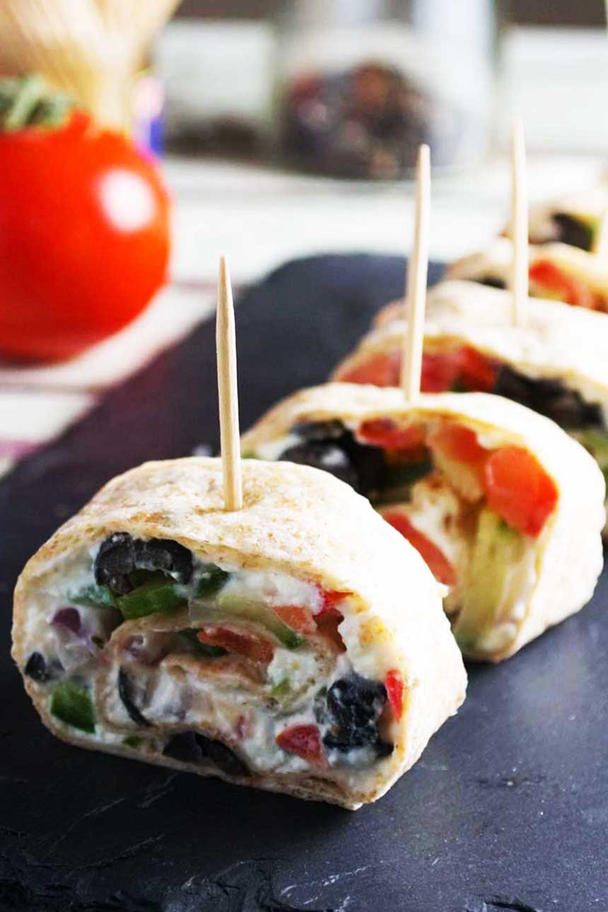 A close up of Greek tortilla pinwheels on a black slate platter.