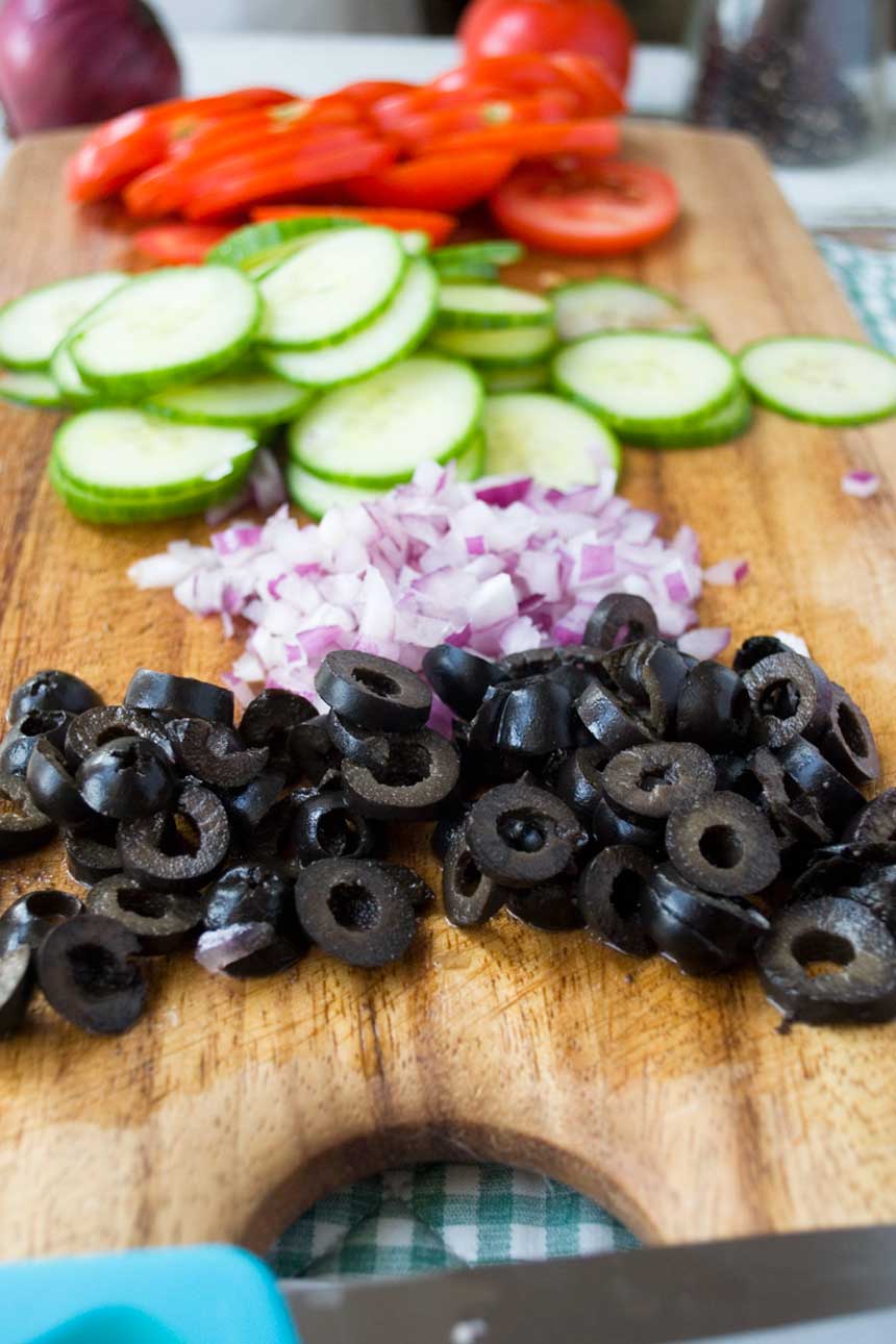 Ingredients to make Greek style tortilla pinwheels on a wooden board.
