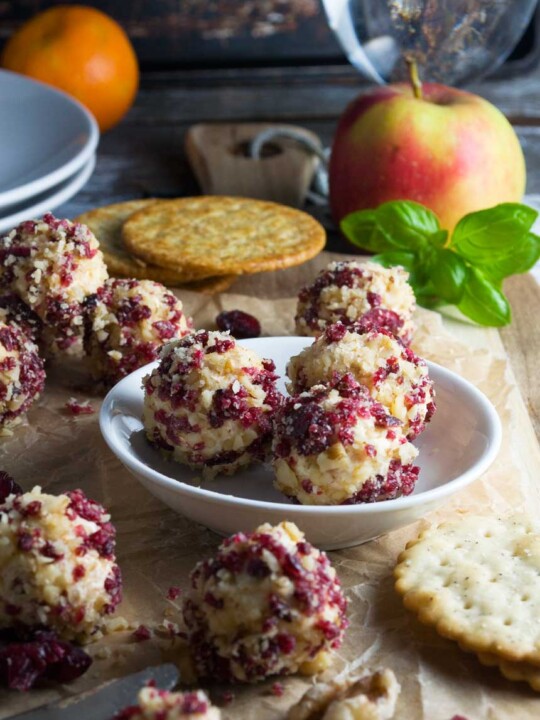 A close up of cranberry and walnut cheese truffles on a small plate with more truffles and crackers in the background.