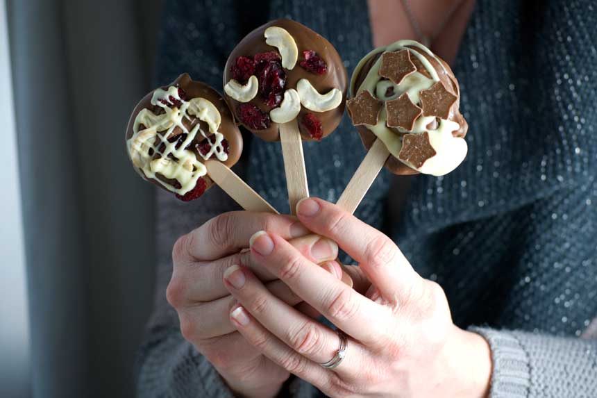 Someone holding up 3 different decorated chocolate lollipops.