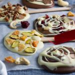 Homemade chocolate lollipops decorated in different ways lined up on baking paper and a blue cloth.