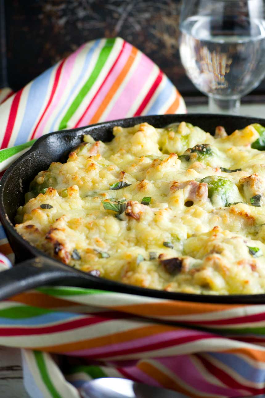 A cast iron pan with baked Christmas macaroni cheese in it - there\'s a striped tea towel in the background