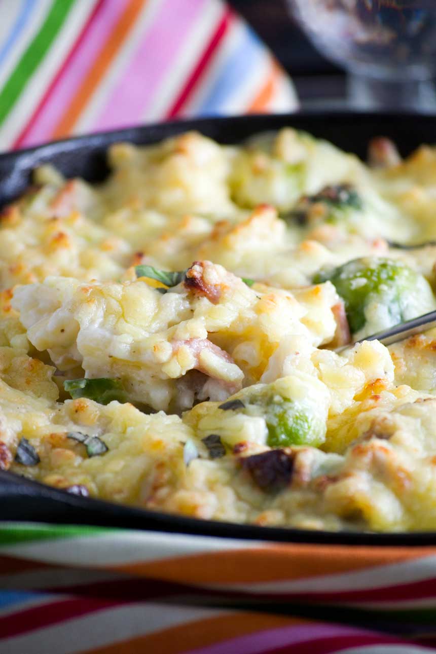 Close up of someone lifting a spoonful of Christmas macaroni cheese from a cast iron pan