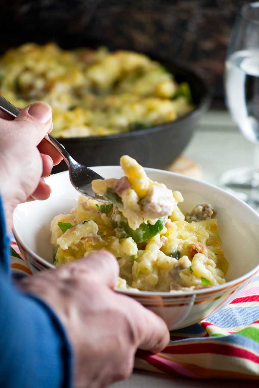 Someone holding a bowl of Christmas macaroni cheese and eating it with a fork - the baking dish is in the background