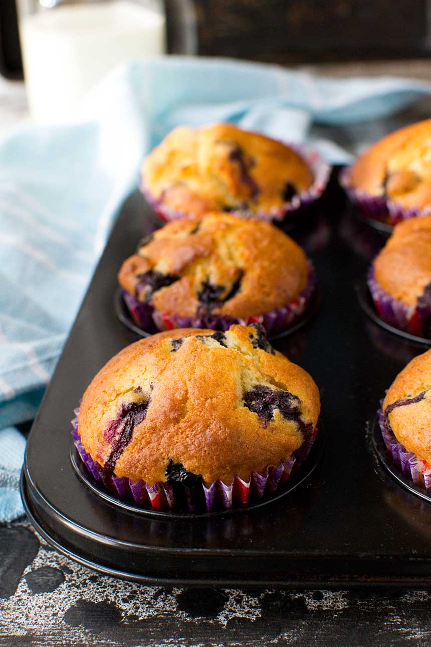 Greek yogurt blueberry muffins just baked in the muffin pan with a blue tea towel next to it.