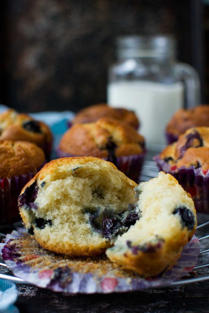 The inside of a Greek yogurt blueberry muffin on a cooling rack with more muffins