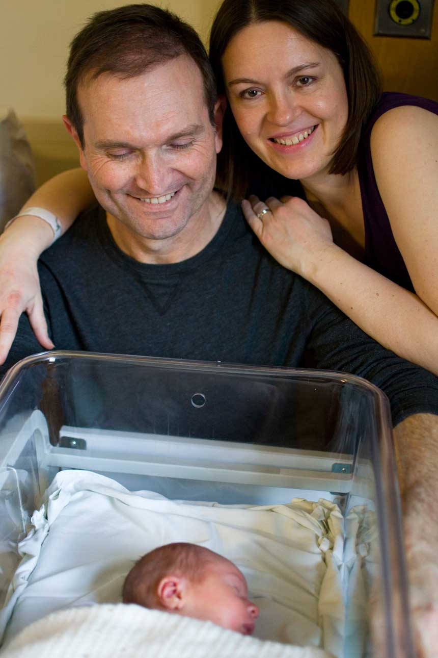 A couple with their arms around each other watching over a newborn baby.