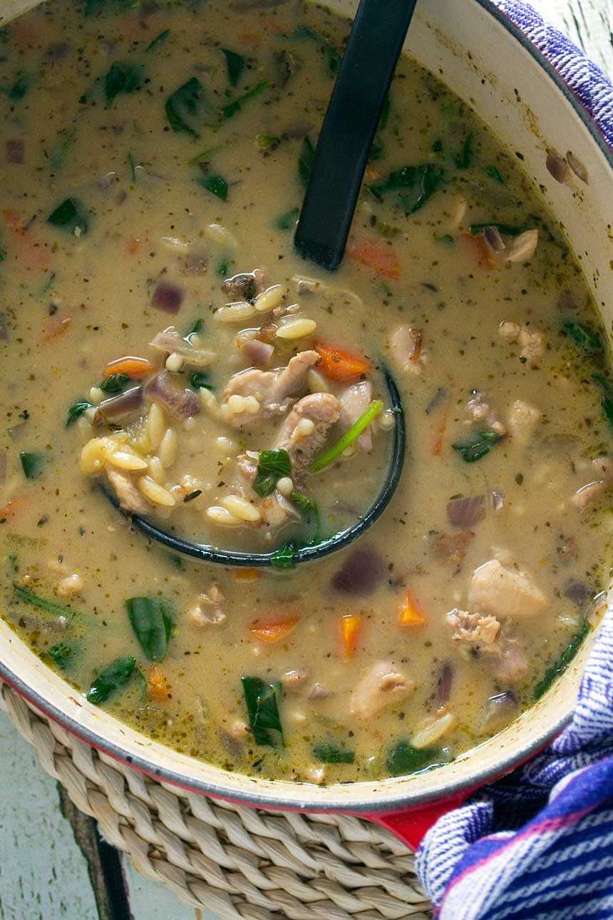 Closeup of creamy lemon chicken orzo soup in a pot from above with a black ladle in it.