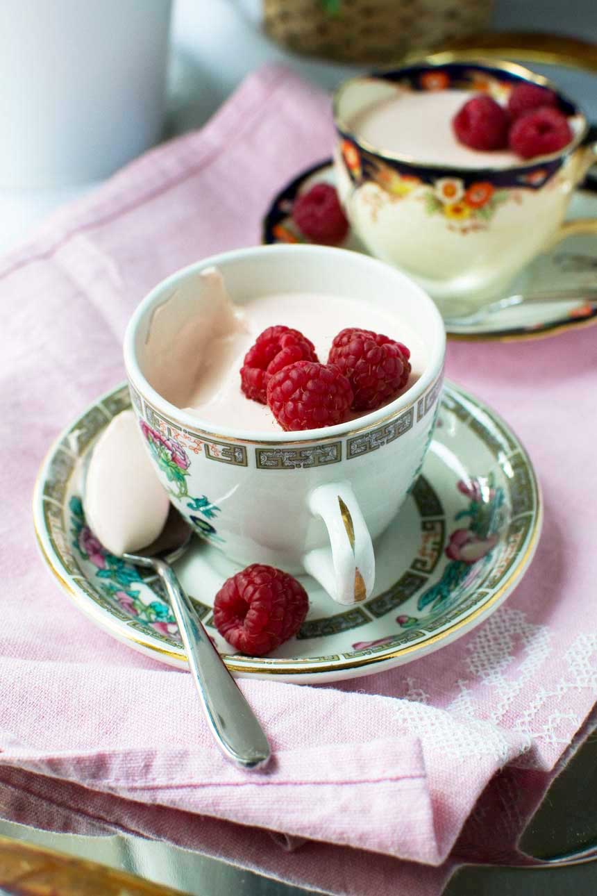 Raspberry Greek yogurt panna cotta in a pretty tea cup on a pink background.