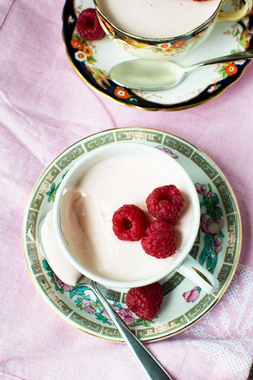 Raspberry Greek yogurt panna cotta with raspberries on top in a pretty tea cup from above and on a pink background.