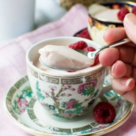 Someone spooning raspberry Greek yogurt panna cotta out of a pretty tea cup on a pink cloth.