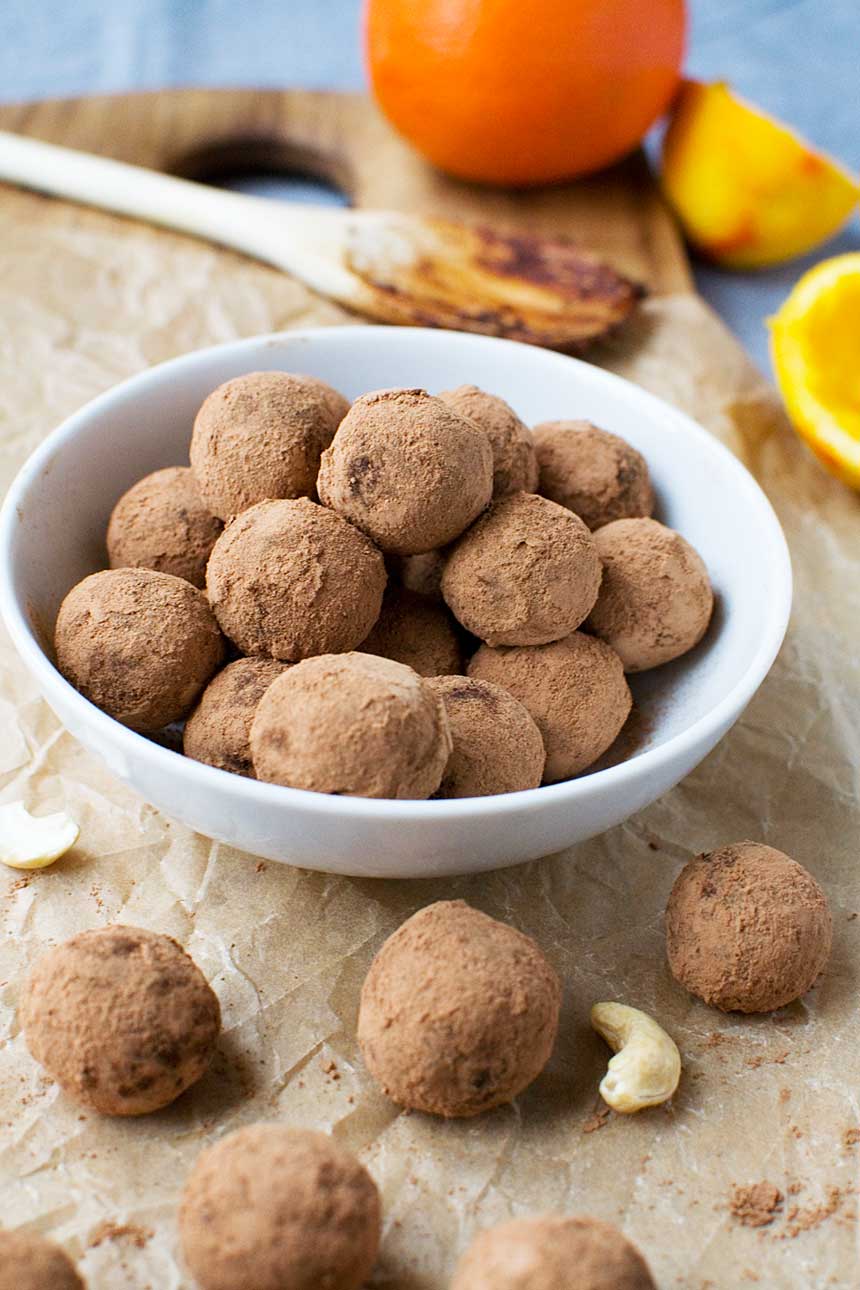 5-ingredient healthy chocolate orange truffles stacked in a small white bowl with more truffles and kitchen all around