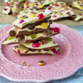 A stack of Easter chocolate bark on a decorative pink plate with more bark in the background.