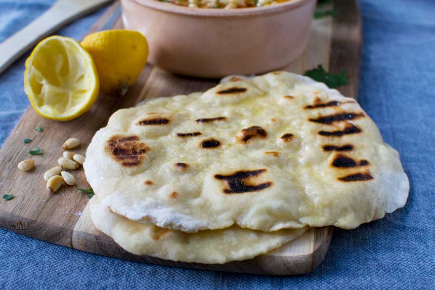 A slice of pizza sitting on top of a wooden cutting board, with Hummus and Bread