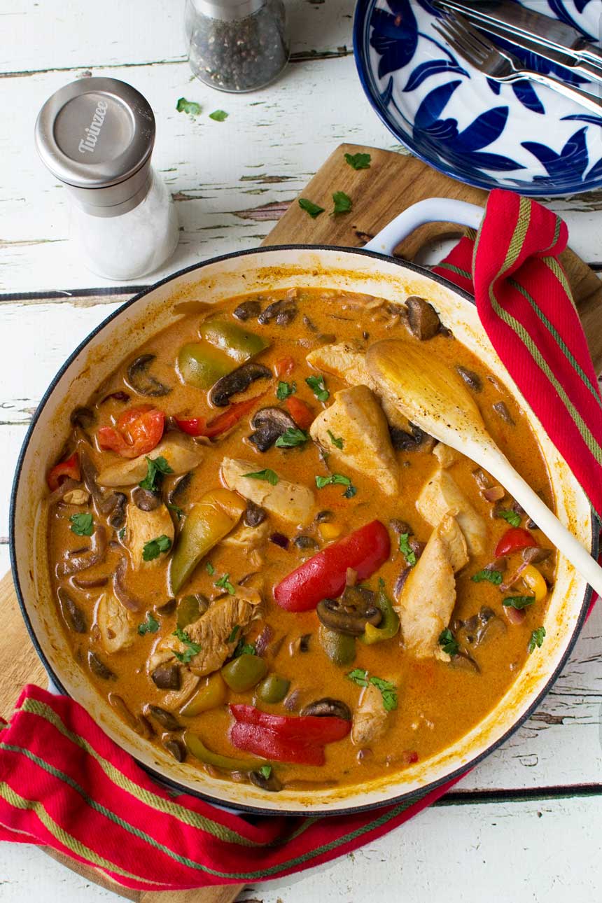 Paprika chicken in a cast iron pan from above on a wooden board and with a red tea towel.