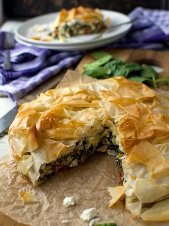 Closeup of a spinach and feta filo pie on baking paper with a piece cut out.
