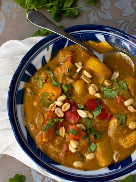 A closeup of a blue bowl of Thai Massaman chicken curry with sweet potato and peanuts taken from above.