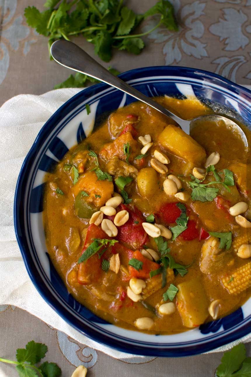 A closeup of a blue bowl of Thai Massaman chicken curry with sweet potato and peanuts taken from above.