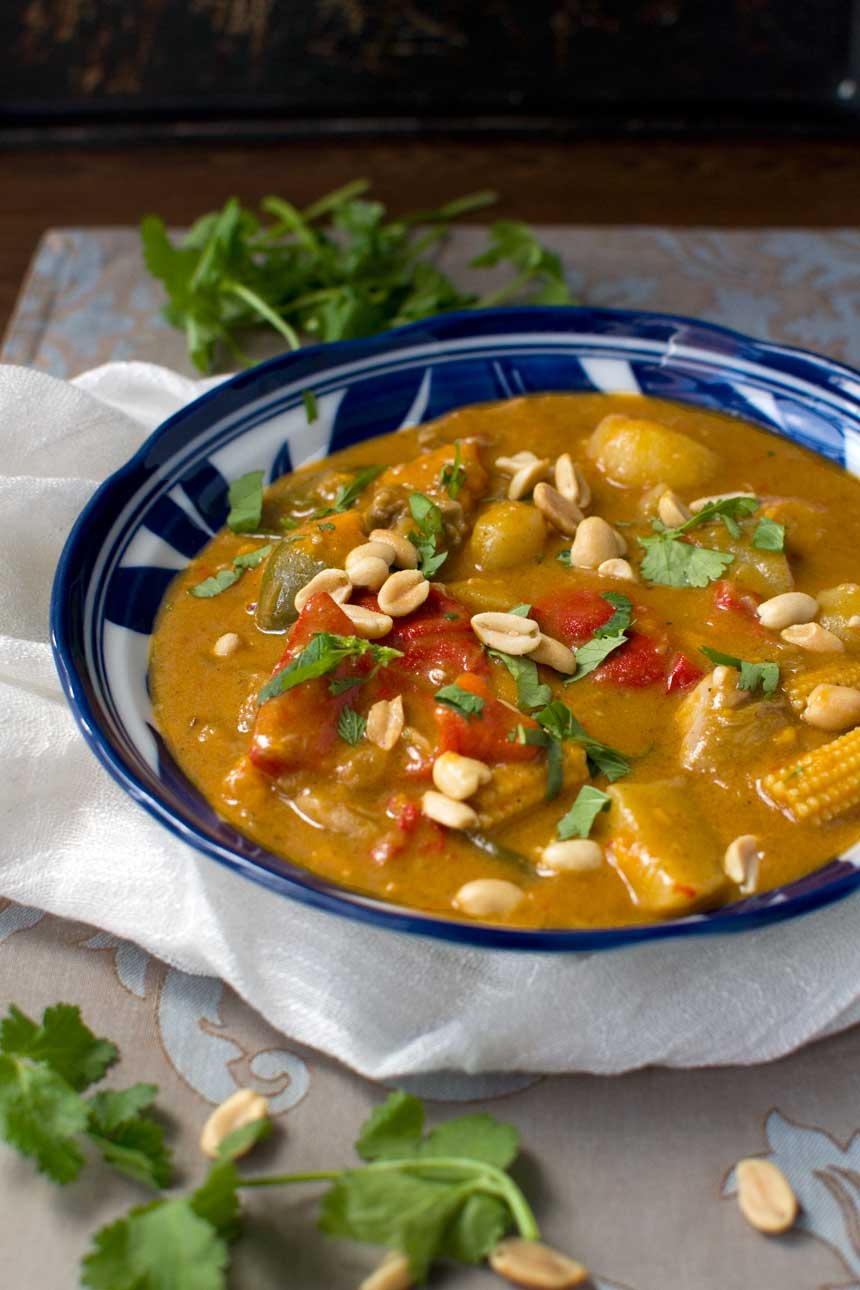 A blue bowl of Thai Massaman chicken curry with sweet potato and peanuts on a cream cloth.