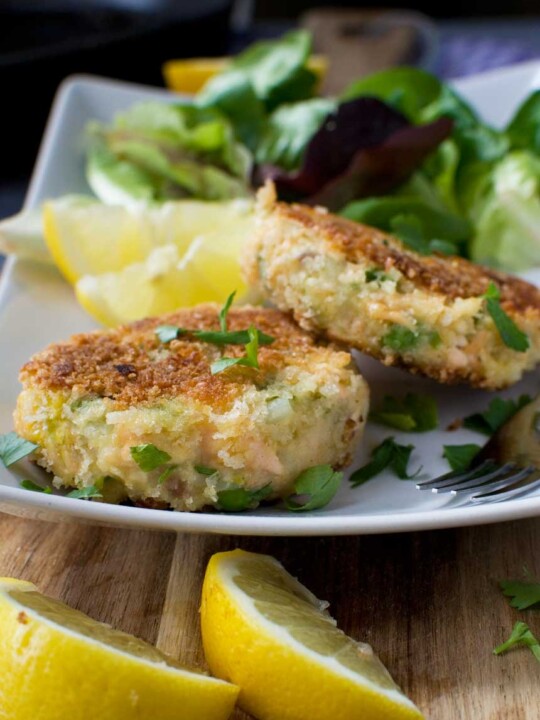 Basic crispy salmon fishcakes on a rectangular plate with salad and lemon wedges in the background