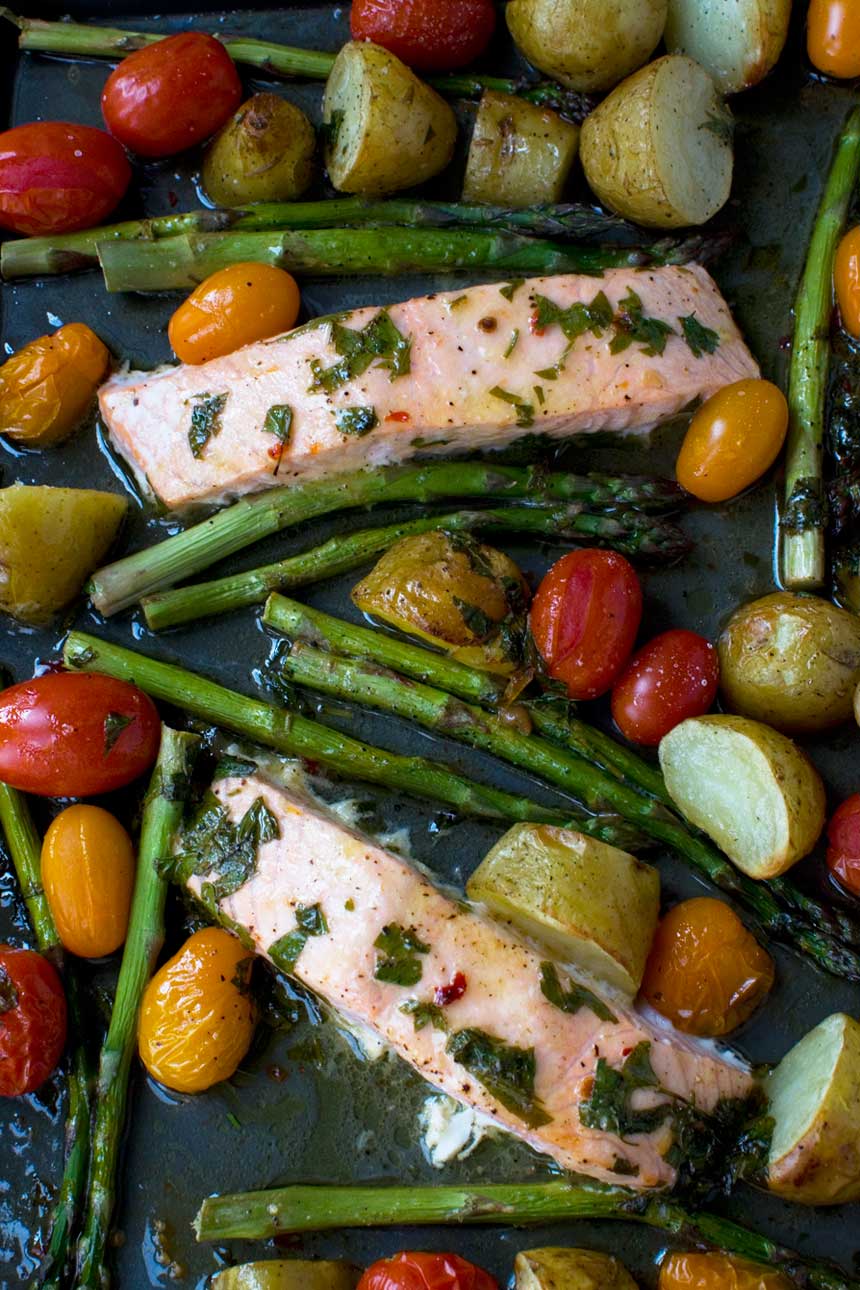 A close up of lemon butter salmon and vegetables on a sheet pan from above.