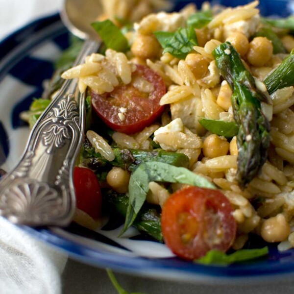 Closeup of an Asparagus, tomato and feta orzo salad in a blue patterned dish and with a patterned serving spoon.