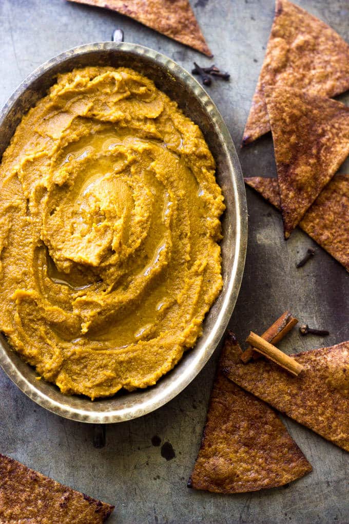 A bowl of pumpkin hummus with tortilla chips from above.