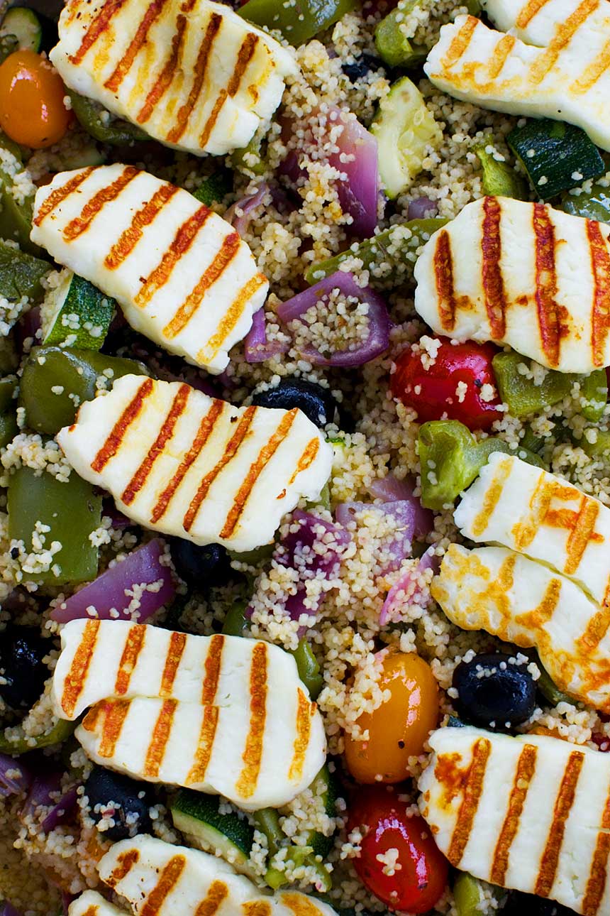 closeup of pan-fried halloumi with grill lines on it on top of couscous and roasted vegetables from above