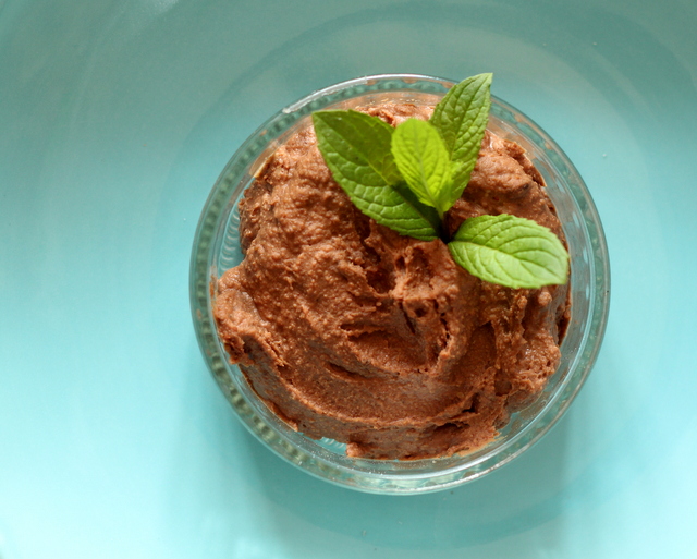 A small bowl of chocolate hummus with a sprig of mint in it on a green background.