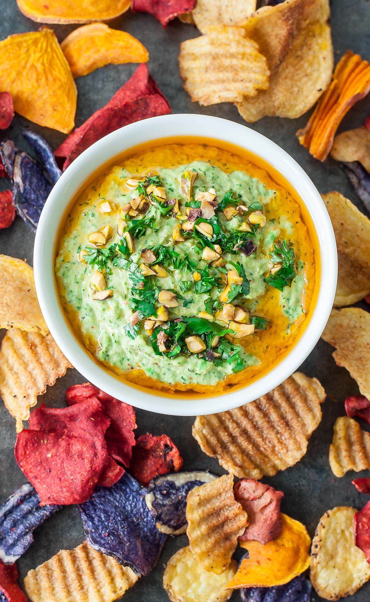 Bowl of Cilantro, pea and pistachio hummus with veggie chips around it from above.