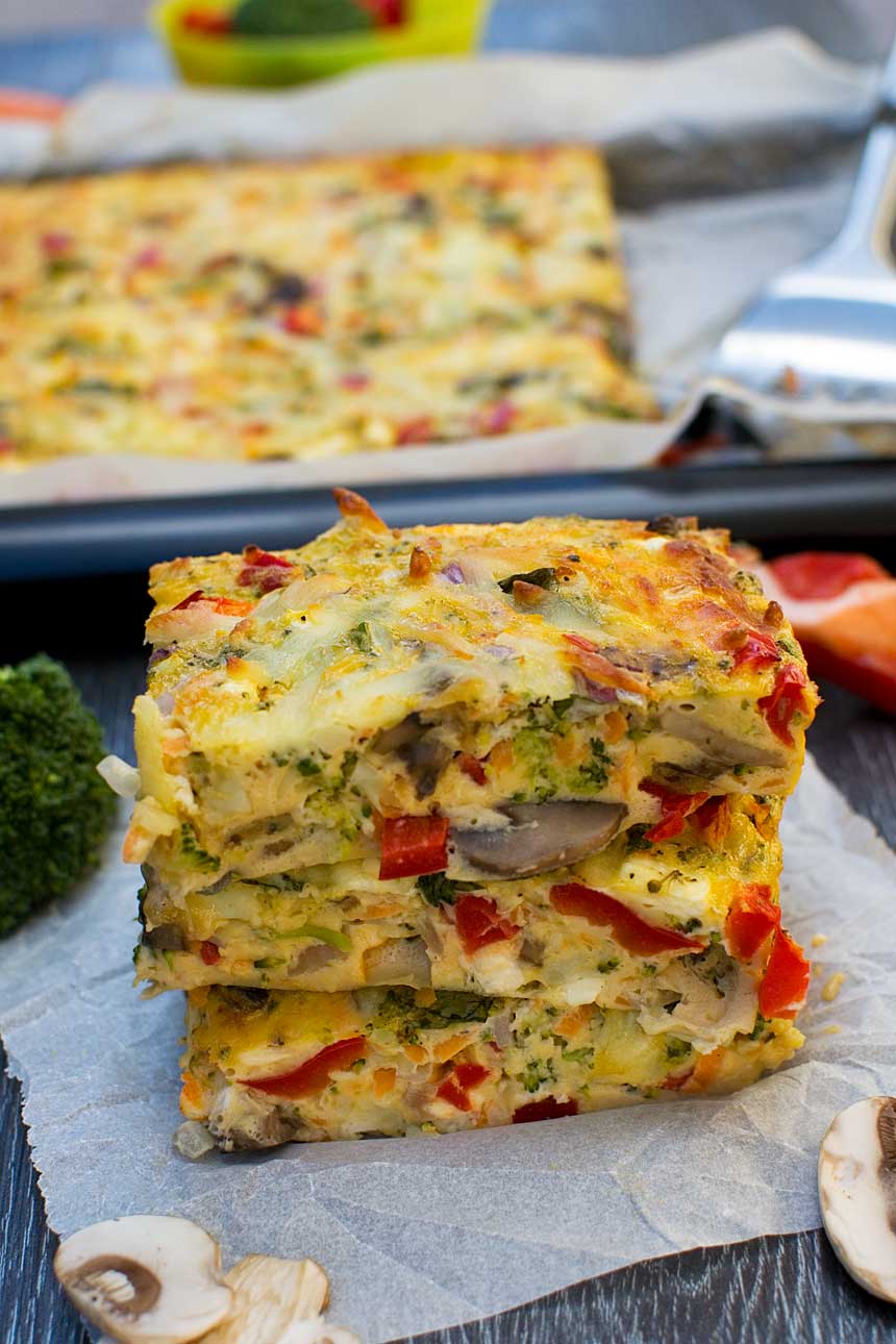 A small stack of pieces of sheet pan frittata on baking paper and with the rest of the pan of food in the background.