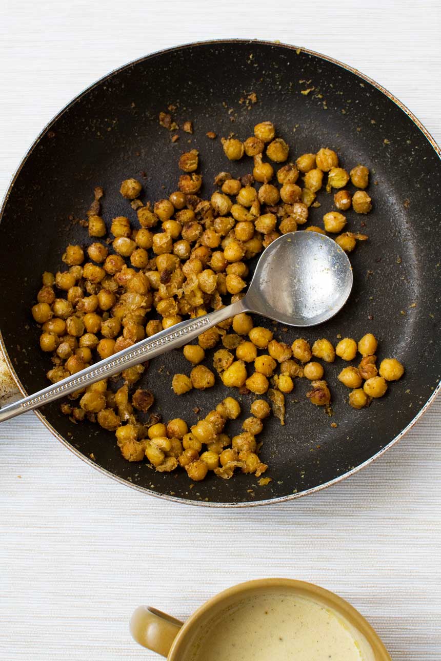 Crispy fried chickpeas just cooked in a frying pan with a metal spoon