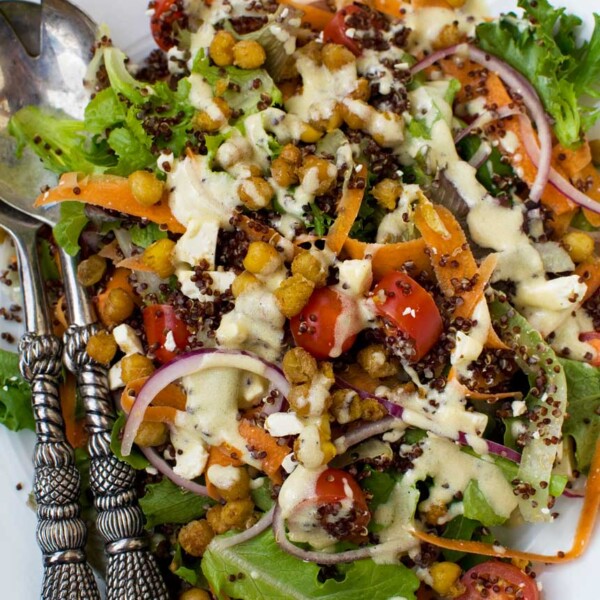 A plate of crispy fried chickpeas sprinkled on a salad from above with decorative salad servers