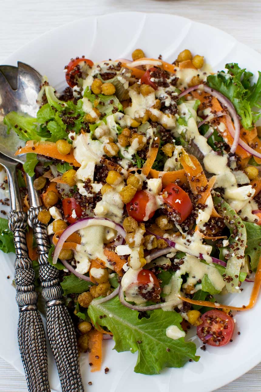 A plate of crispy fried chickpeas sprinkled on a salad from above with decorative salad servers