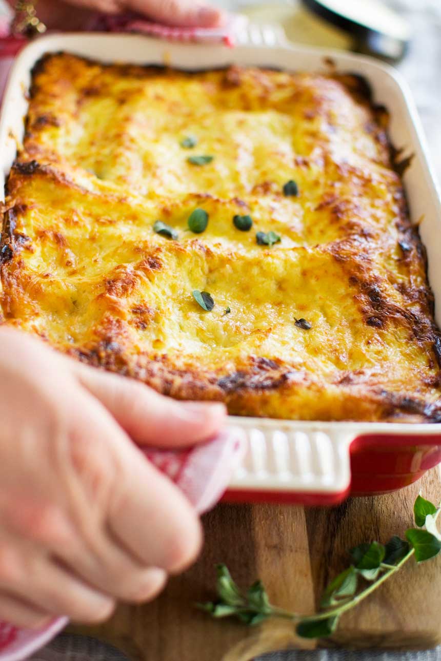 A close up of a person holding a baking dish with an eggplant lasagna in it